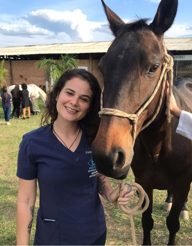 Dra. Fab&iacute;ola ao lado de cavalo em ambiente externo
